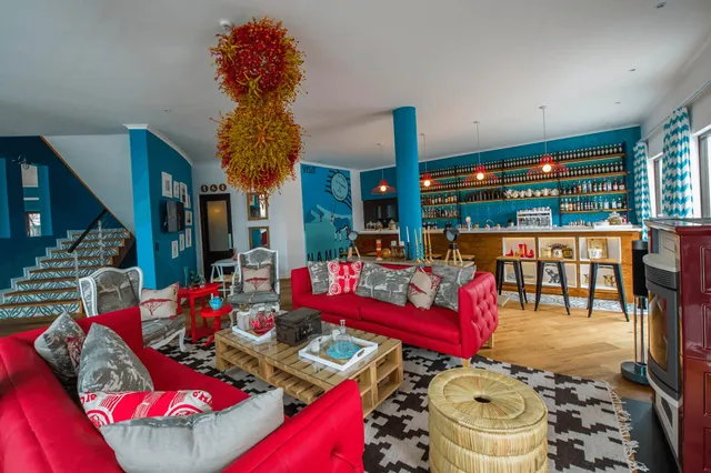 Weite Innenaufnahme einer bunten Lounge mit rotem Sofa, Holztisch und Bar im Hintergrund