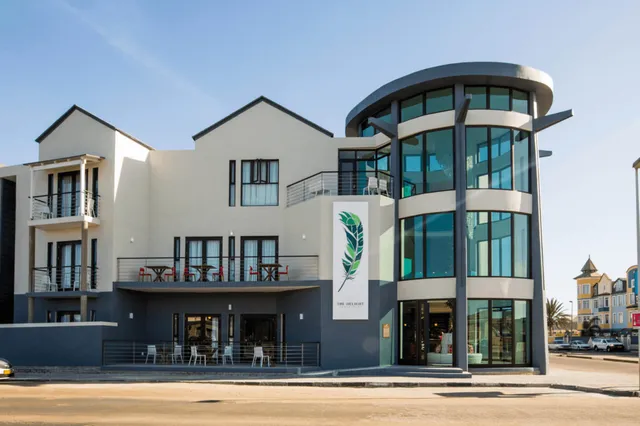 Modernes Gebäude mit rundem Glasturm, Balkonen und Terrasse bei sonnigem Tageslicht