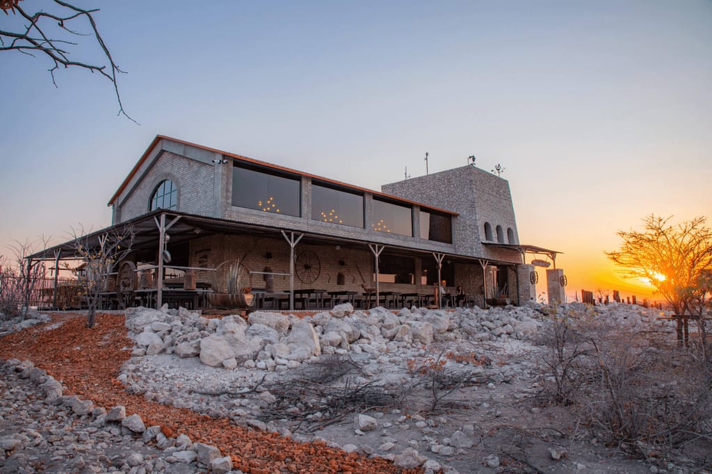 Steinbau mit Veranda in trockener, steiniger Landschaft bei warmem Sonnenuntergang