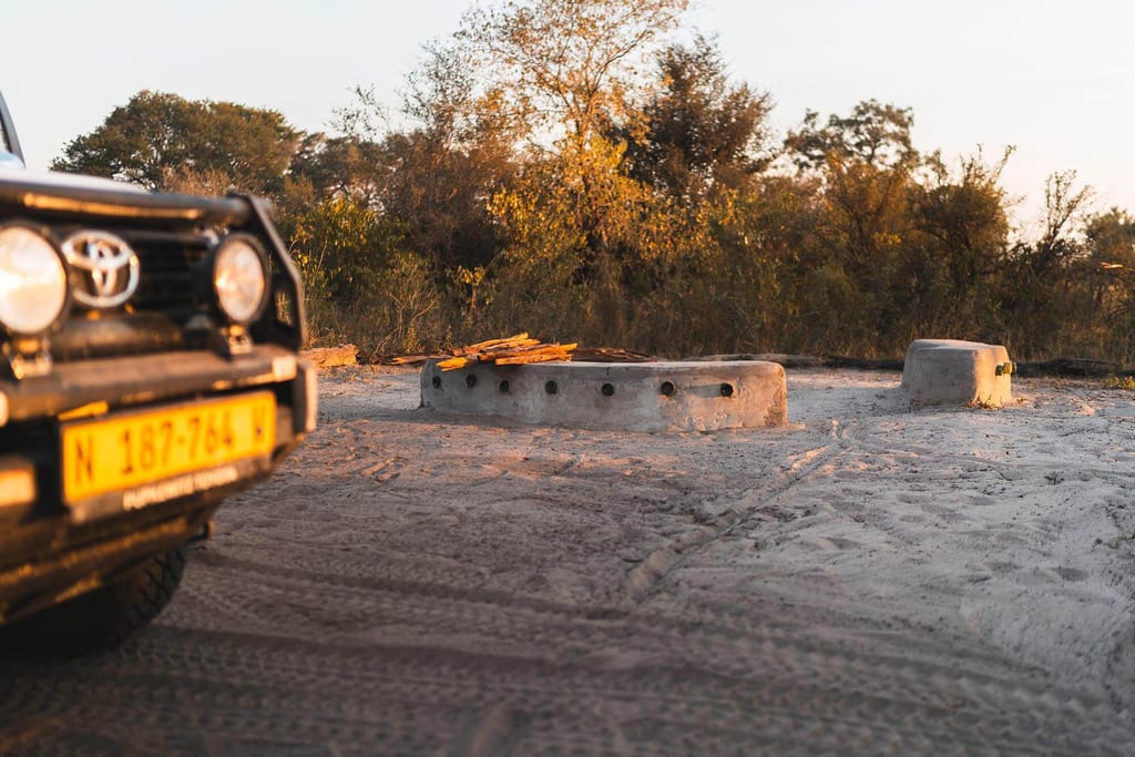 Teilansicht eines Geländewagens und Betonstrukturen auf sandigem Boden im warmen Abendlicht.