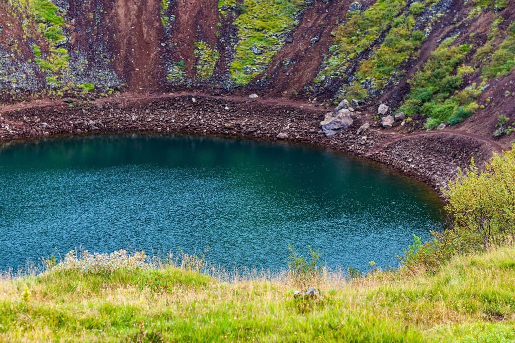 Türkisfarbener Kratersee in steilen, grasbewachsenen Hängen bei diffusem Tageslicht.