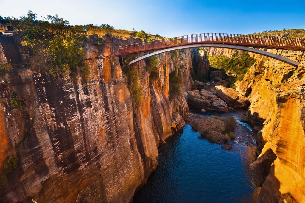Bogenbrücke über tiefe Felsenschlucht mit Fluss, warme Abendstimmung, Blick von oben