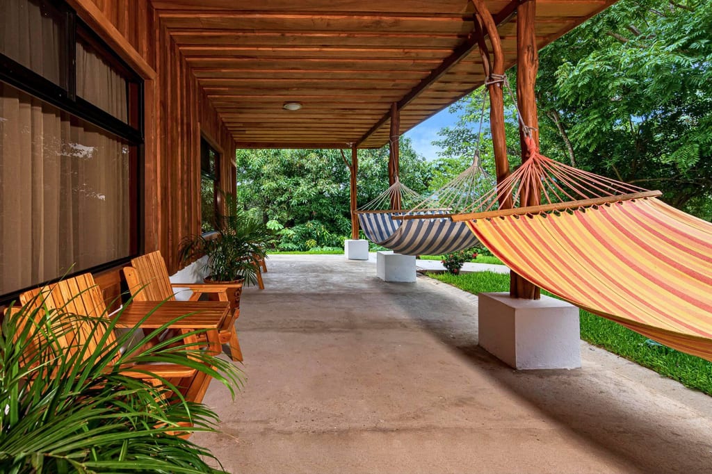 Überdachte Veranda mit bunten Hängematten, Holzstühlen und Blick in einen grünen Garten