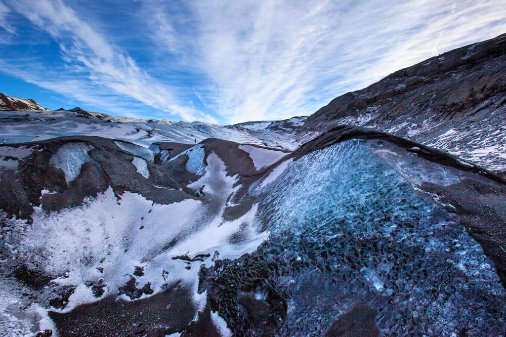 Weite Gletscherlandschaft mit blauem Eis, dunklen Ablagerungen und streifigem Himmel aus tiefem Blickwinkel