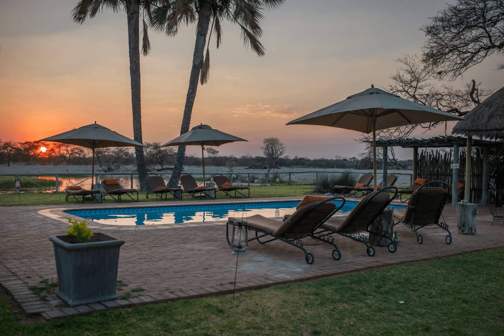 Pool mit Liegen und Sonnenschirmen am Seeufer bei Sonnenuntergang, ruhige Abendstimmung.