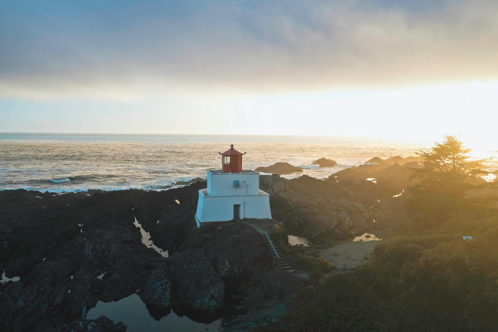 Kleiner weißer Leuchtturm auf Felsen an der Küste bei Sonnenuntergang, warmes Seitenlicht