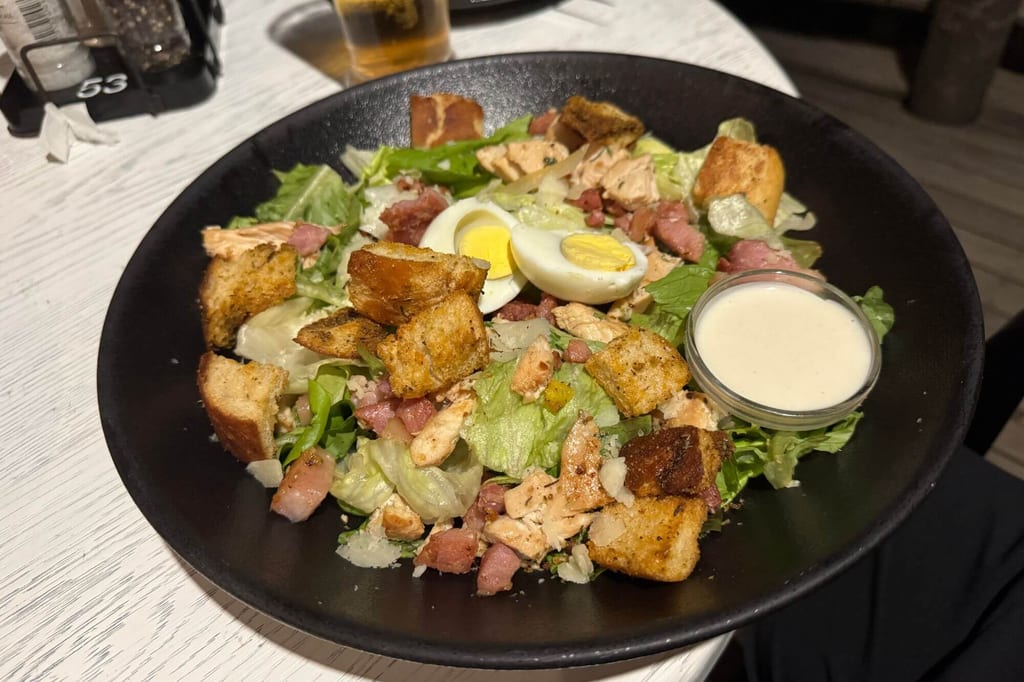 Nahaufnahme eines gemischten Salats mit Croutons, Ei, Speckwürfeln und Dressing in schwarzer Schale