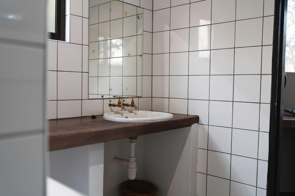 Schlichtes Badezimmer mit weiß gefliesten Wänden, Waschbecken, Messing-Hahn und Spiegel
