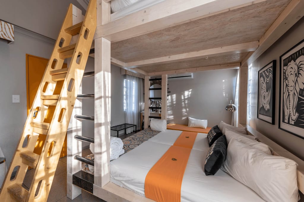 Innenraum mit massivem Etagenbett, Leiter, weißen Betten und orangefarbenen Läufern bei Tageslicht