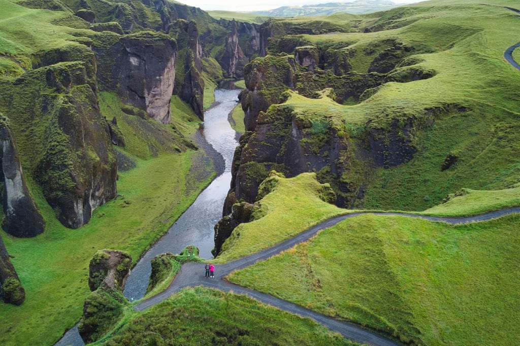 Luftbild einer moosgrünen Schlucht mit Fluss, Wanderwegen und zwei Personen in der Landschaft.