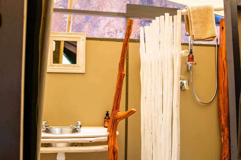 Rustikales Glamping-Badezimmer mit Waschbecken, Dusche und Holzdetails bei Tageslicht.