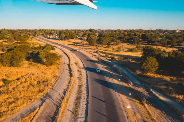 Luftaufnahme einer Straße bei Maun, Botswana mit vereinzelten Fahrzeugen und goldener Savanne im Spätnachmittagslicht.