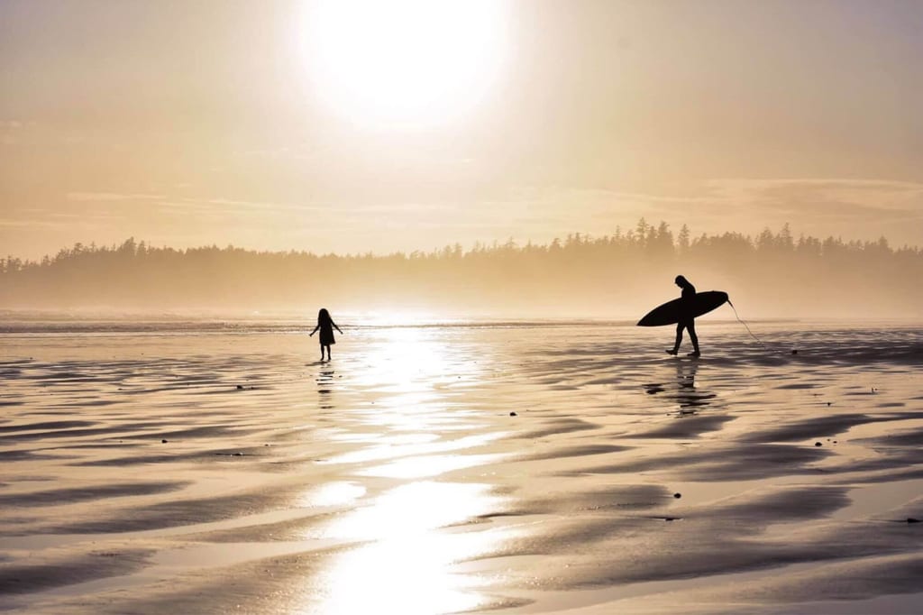 Ein Surfer steht an einem langen Sandstrand in Tofino