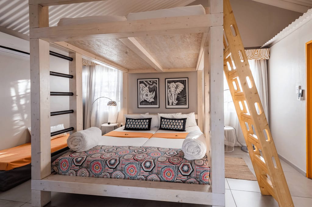 Helles Schlafzimmer mit Holz-Hochbett, Doppelbett darunter, gemusterter Bettdecke und Leiter