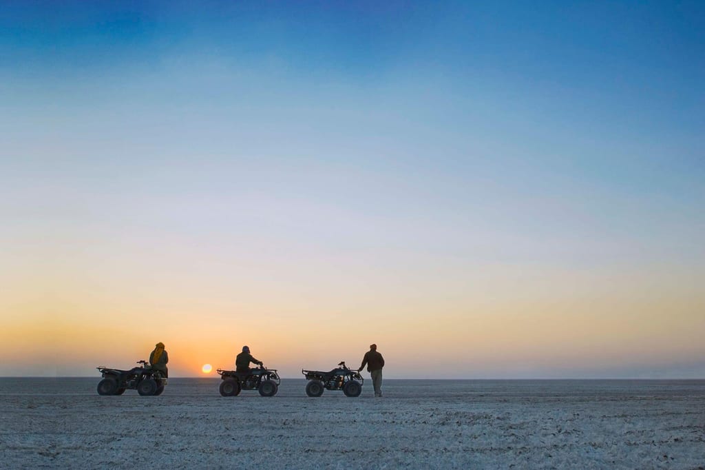 Drei Quads und drei Personen auf weiter, flacher Ebene bei tiefstehender Sonne