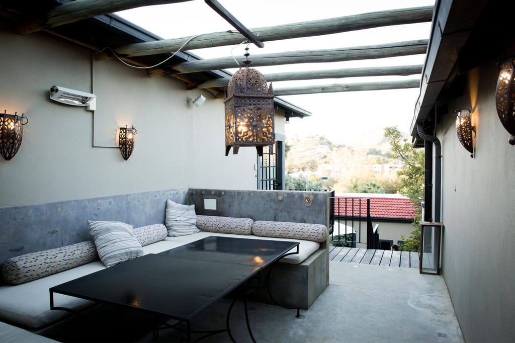 Überdachte Terrasse mit Betonbank, Kissen, niedrigem Tisch und dekorativer Hängelaterne bei Abendlicht.