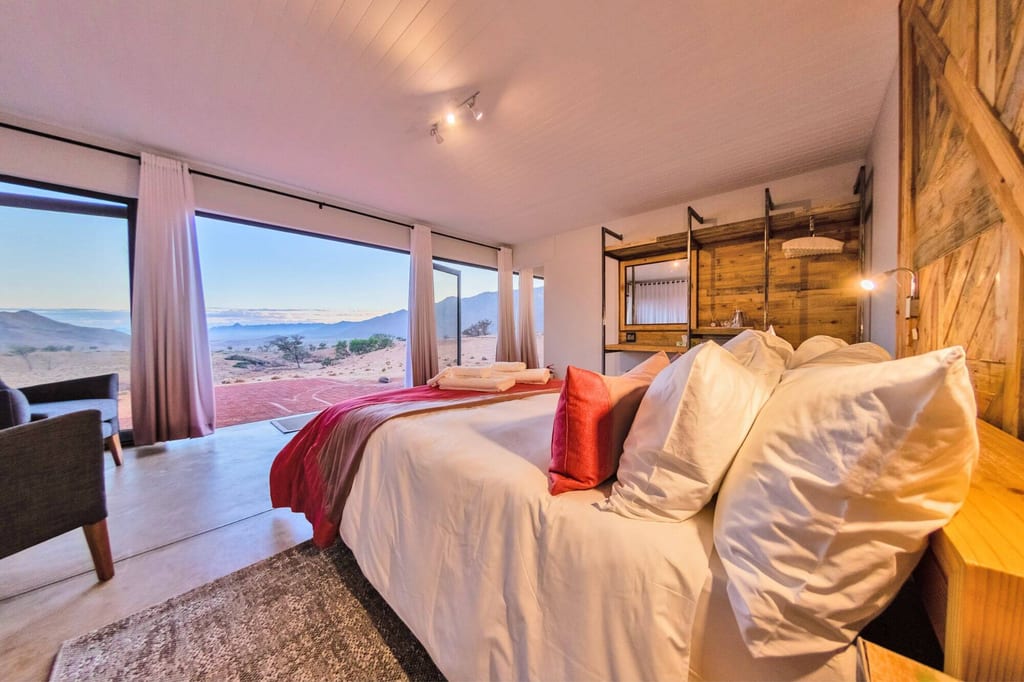 Gemütliches Schlafzimmer mit großem Bett und Panoramafenstern zur Wüstenlandschaft bei warmem Licht.