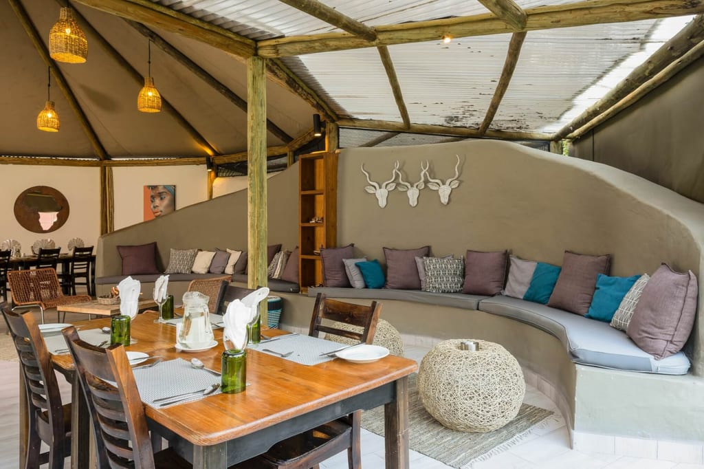 Gemütliche Lodge-Lounge mit geschwungener Polsterbank, bunten Kissen und gedeckten Holztischen