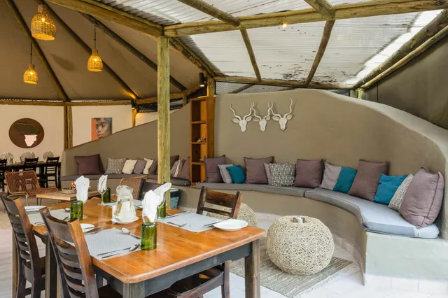 Gemütliche Lodge-Lounge mit geschwungener Polsterbank, bunten Kissen und gedeckten Holztischen