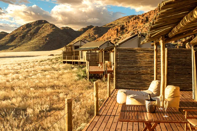 Veranda einer Lodge mit Sitzsäcken vor goldener Grassteppe und bergigen Hügeln im Abendlicht