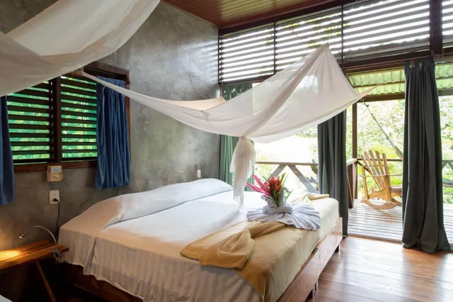 Helles Schlafzimmer mit Doppelbett, Moskitonetz und offener Terrassentür zur grünen Außenvegetation.