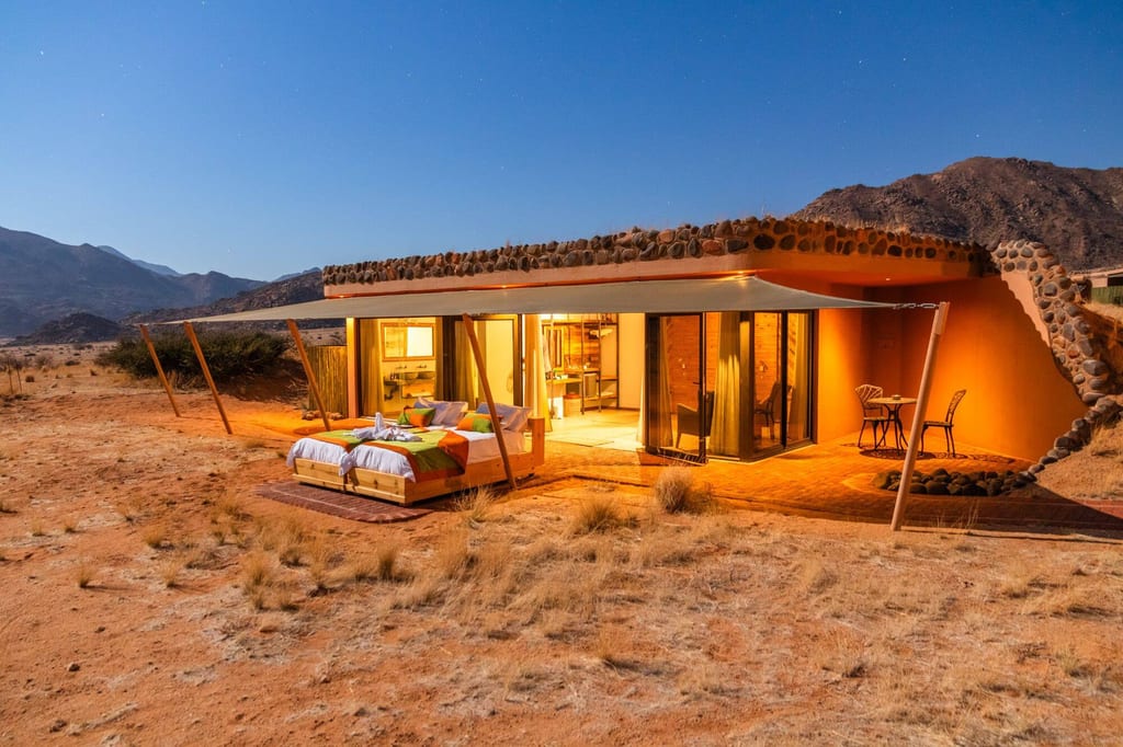 Wüstenlodge mit Betten auf der Veranda, warm beleuchtet unter Sternenhimmel