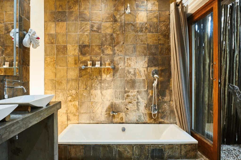 Rustikales Badezimmer mit Badewanne, Natursteinfliesen, Holzwaschtisch und großer Glasschiebetür