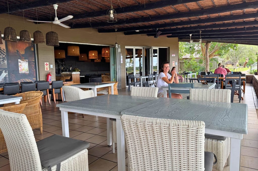 Überdachte Restaurantterrasse mit Tischen, Korbstühlen und entspannter Tageslichtstimmung.