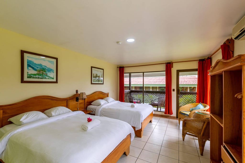 Helles Hotelzimmer mit zwei Doppelbetten, Balkon und roten Vorhängen