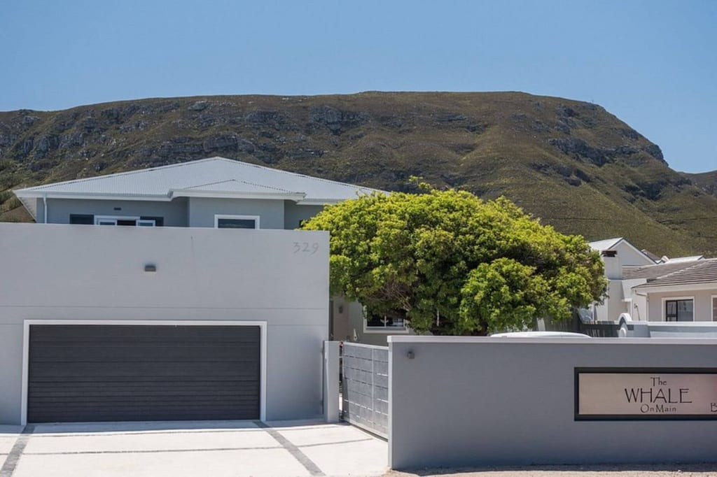 Modernes Wohnhaus mit Garage, Baum und Berg im Hintergrund bei hellem Tageslicht.