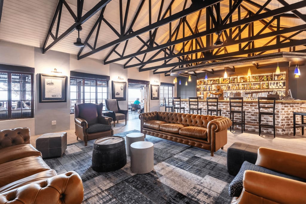 Gemütliche Lounge mit Ledersofas, Bar und sichtbaren Dachbindern, warm beleuchtet.