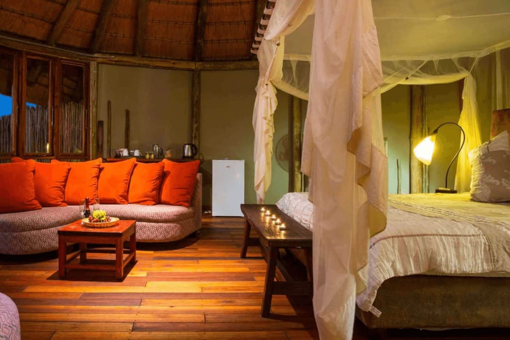 Gemütliches Lodge-Zimmer mit Moskitonetz, Sofa mit orangefarbenen Kissen und warmem Abendlicht