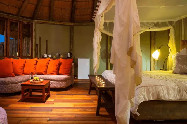 Gemütliches Lodge-Zimmer mit Moskitonetz, Sofa mit orangefarbenen Kissen und warmem Abendlicht