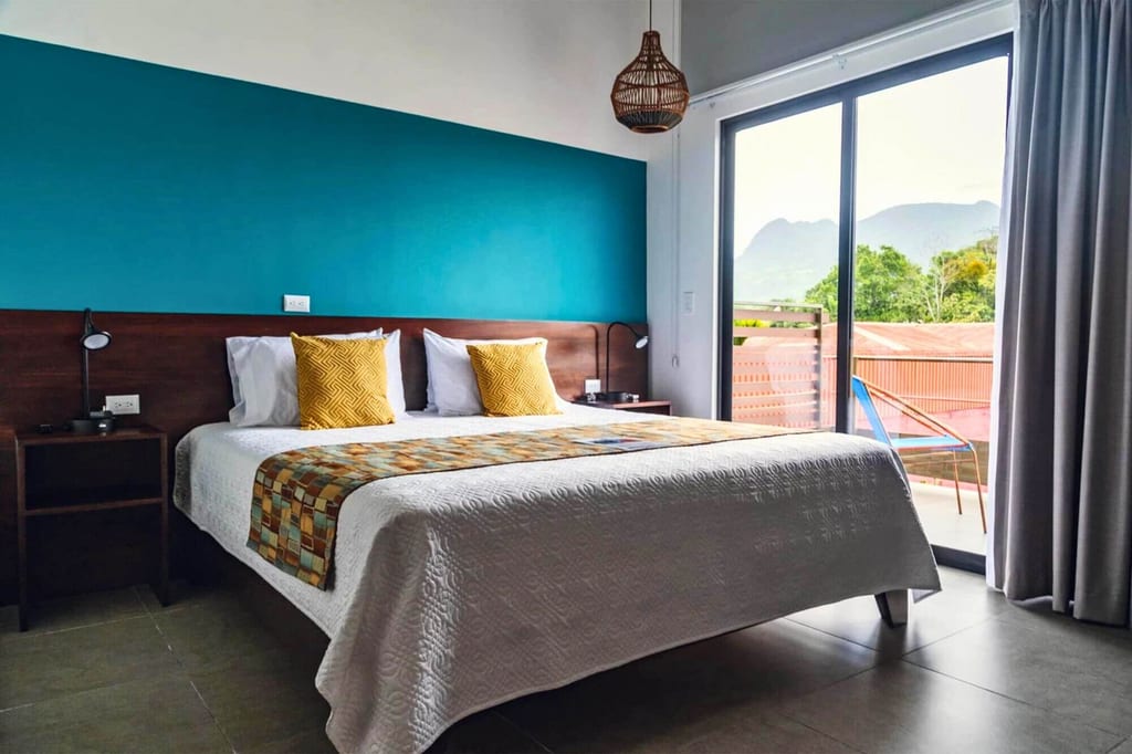 Modernes Schlafzimmer mit Doppelbett, türkisfarbener Wand und Balkonblick zu Bergen