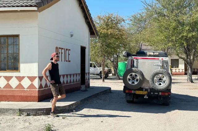 Mann lehnt an Gebäude neben Geländewagen bei hellem Tageslicht.