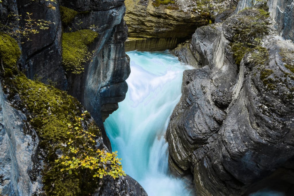 Blick von oben in eine enge Felsenschlucht mit türkisfarbenem Wasser und moosbewachsenen Felsen.