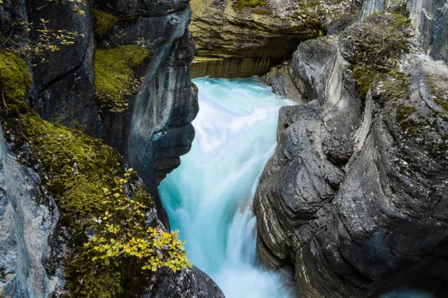 Blick von oben in eine enge Felsenschlucht mit türkisfarbenem Wasser und moosbewachsenen Felsen.