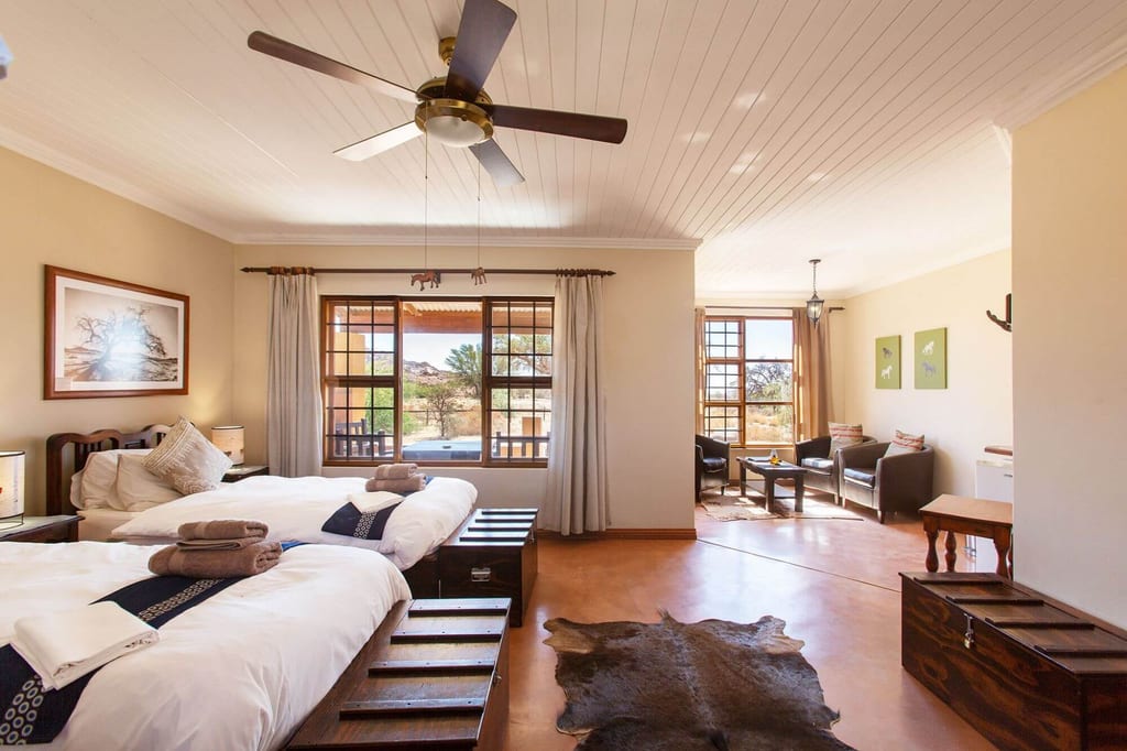 Helles Lodge-Zimmer mit zwei Einzelbetten, Sitzbereich und großen Fenstern mit Landschaftsblick.