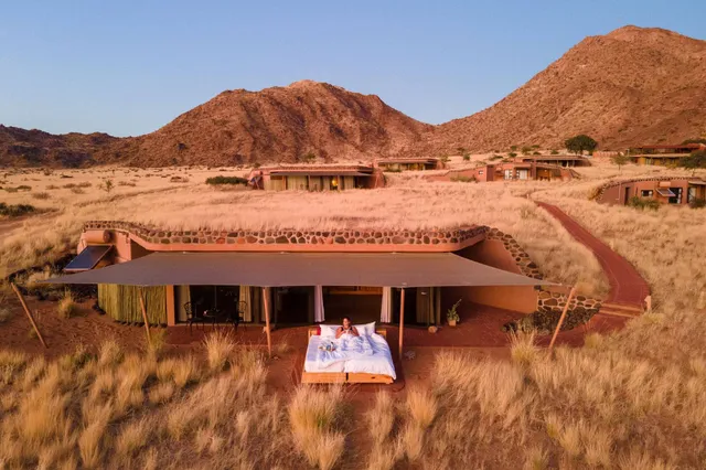 Lodge-Bungalows in Graslandschaft mit offenem Bett auf Terrasse bei goldenem Abendlicht, Luftaufnahme.
