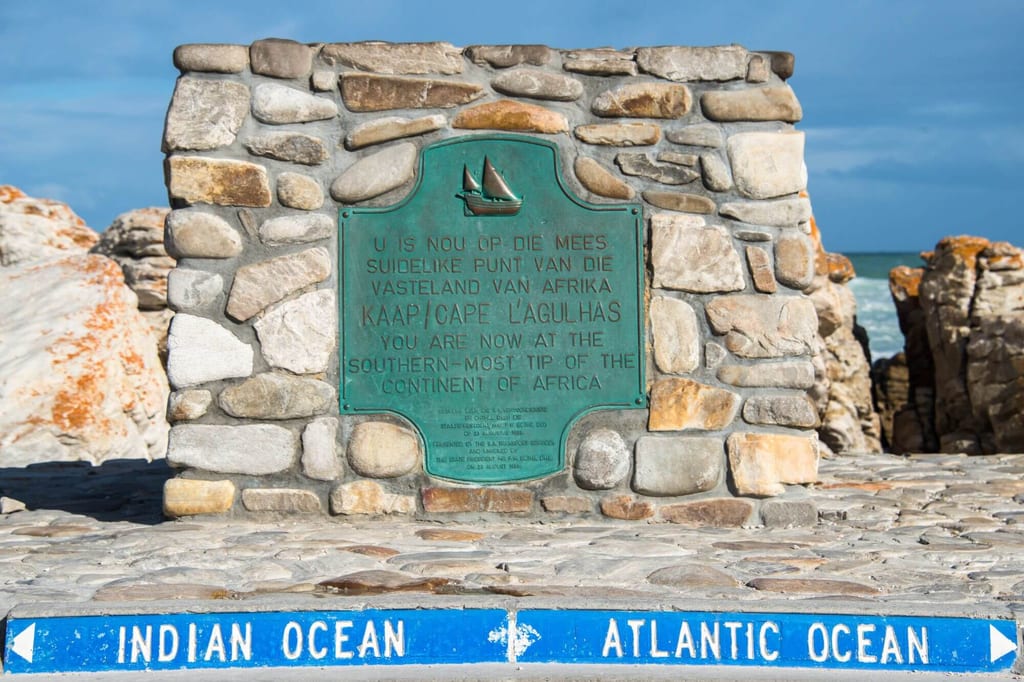 Steinerne Gedenkmauer mit grüner Plakette und Richtungspfeilen zu Indian und Atlantic Ocean