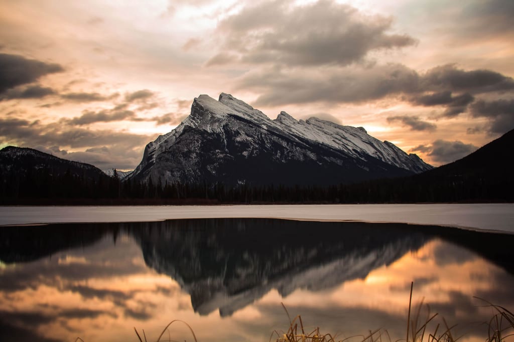 Schneebedeckter Berg spiegelt sich bei wolkigem Abendhimmel in einem ruhigen See