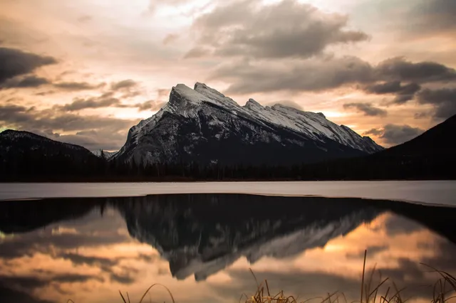 Schneebedeckter Berg spiegelt sich bei wolkigem Abendhimmel in einem ruhigen See