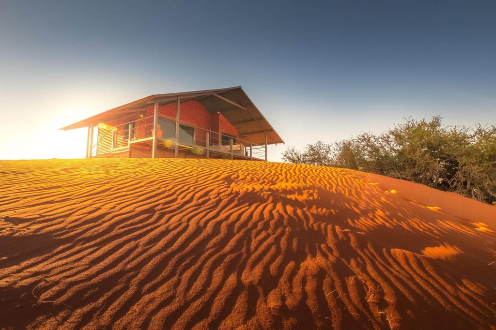 Holzhütte auf roter Sanddüne bei warmem Seitenlicht, niedrige Perspektive