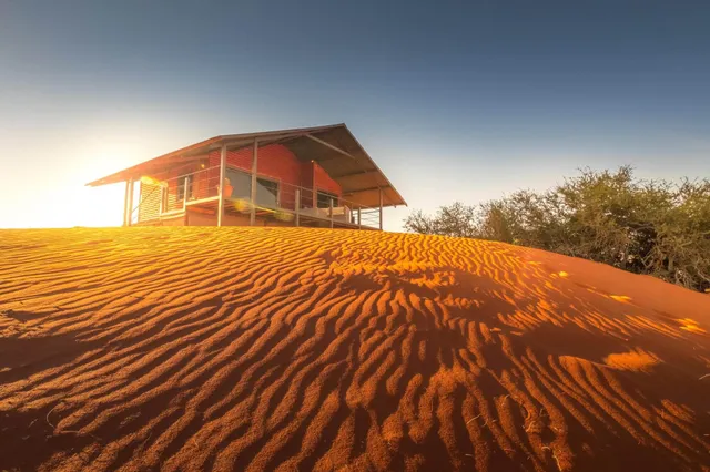 Holzhütte auf roter Sanddüne bei warmem Seitenlicht, niedrige Perspektive