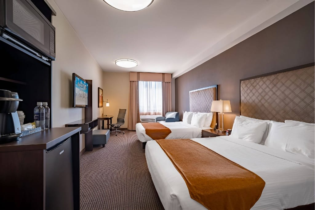 Modernes Hotelzimmer mit zwei Doppelbetten, Schreibtisch und Sitzecke, Tageslicht durchs Fenster