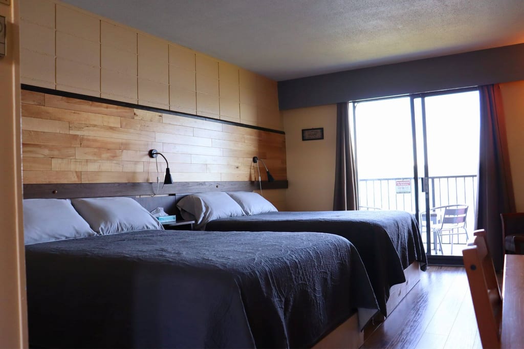 Zweibettzimmer mit zwei Betten, Holz-Headboard und Balkon bei Tageslicht.