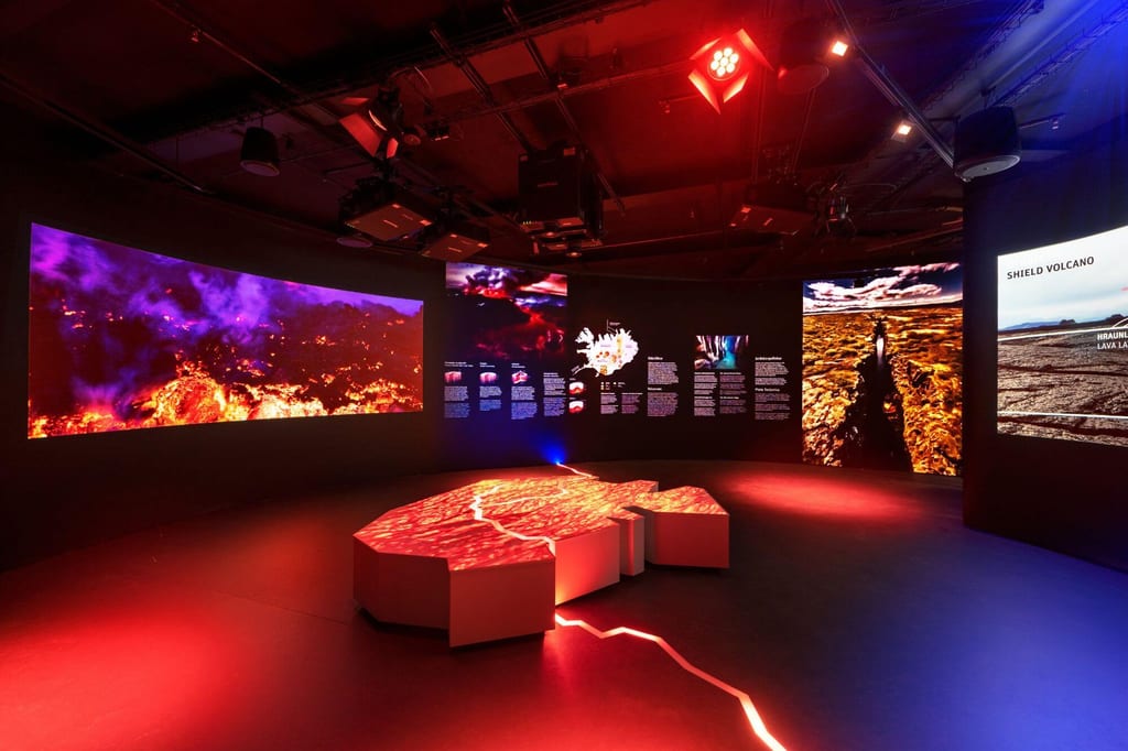 Innenraum einer Ausstellung mit roten Vulkanprojektionen und beleuchteter zentraler Installation