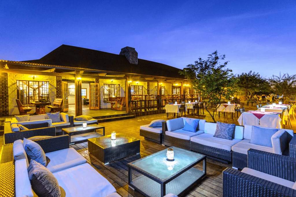 Beleuchtete Lodge-Terrasse mit Sofas und gedeckten Tischen bei Abenddämmerung