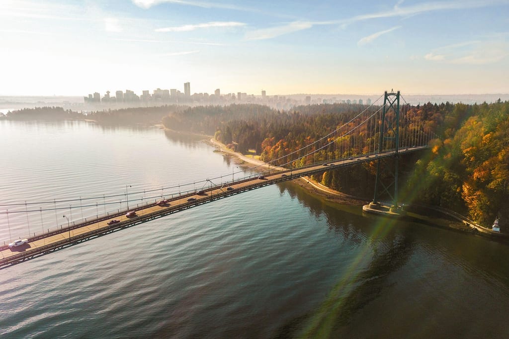 Luftaufnahme der Hängebrücke bei Vancouver mit herbstlichem Küstenwald und Skyline im Morgennebel.