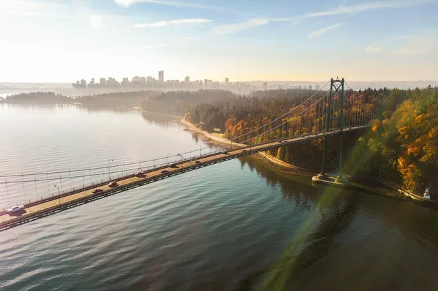 Luftaufnahme der Hängebrücke bei Vancouver mit herbstlichem Küstenwald und Skyline im Morgennebel.